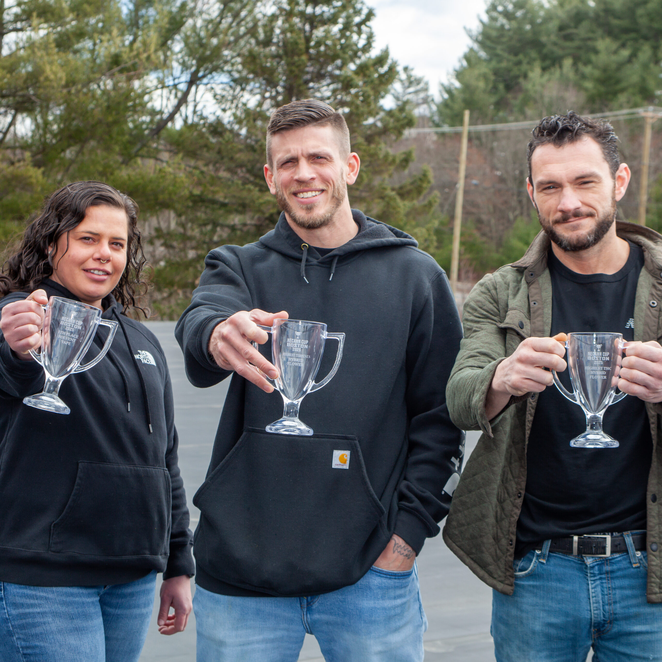 Three people smiling outdoors and holding clear glass trophies in front of them.